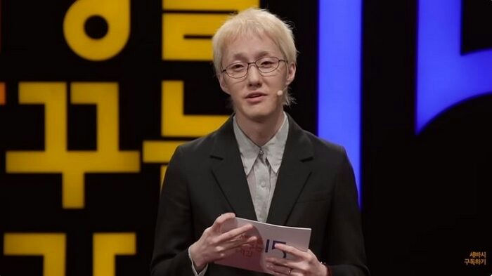 Zion.T self-hate and perfectionismspeaker-glasses-blonde-blacksuit.